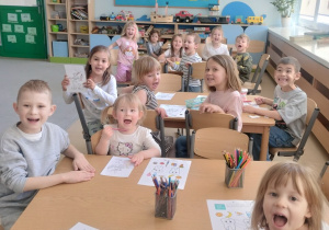 Dzieci z grupy niebieskiej siedząc przy stolikach uśmiechają się pokazując zdrowe zęby