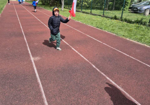 Chłopiec biegnie po bieżni z flagą Polski