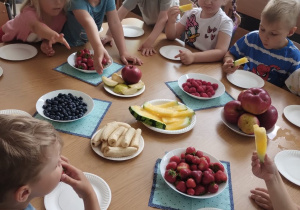 Dzieci siedząc przy stole zjadają owoce