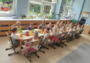 Dzieci siedzą przy stole z poczęstunkiem