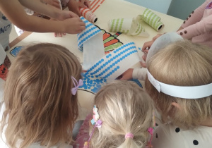 Dzieci współpracują przy pracy plastycznej naklejając drobne kropki na kartonie