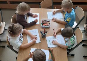 Dzieci siedzą przy stoliku i kolorują kolorowankę