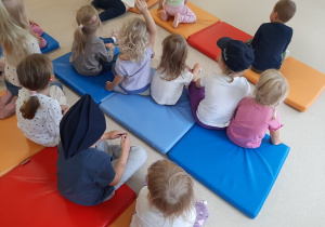 Dzieci siedzą na materacach, dwoje dzieci ma na głowie czapki policyjne